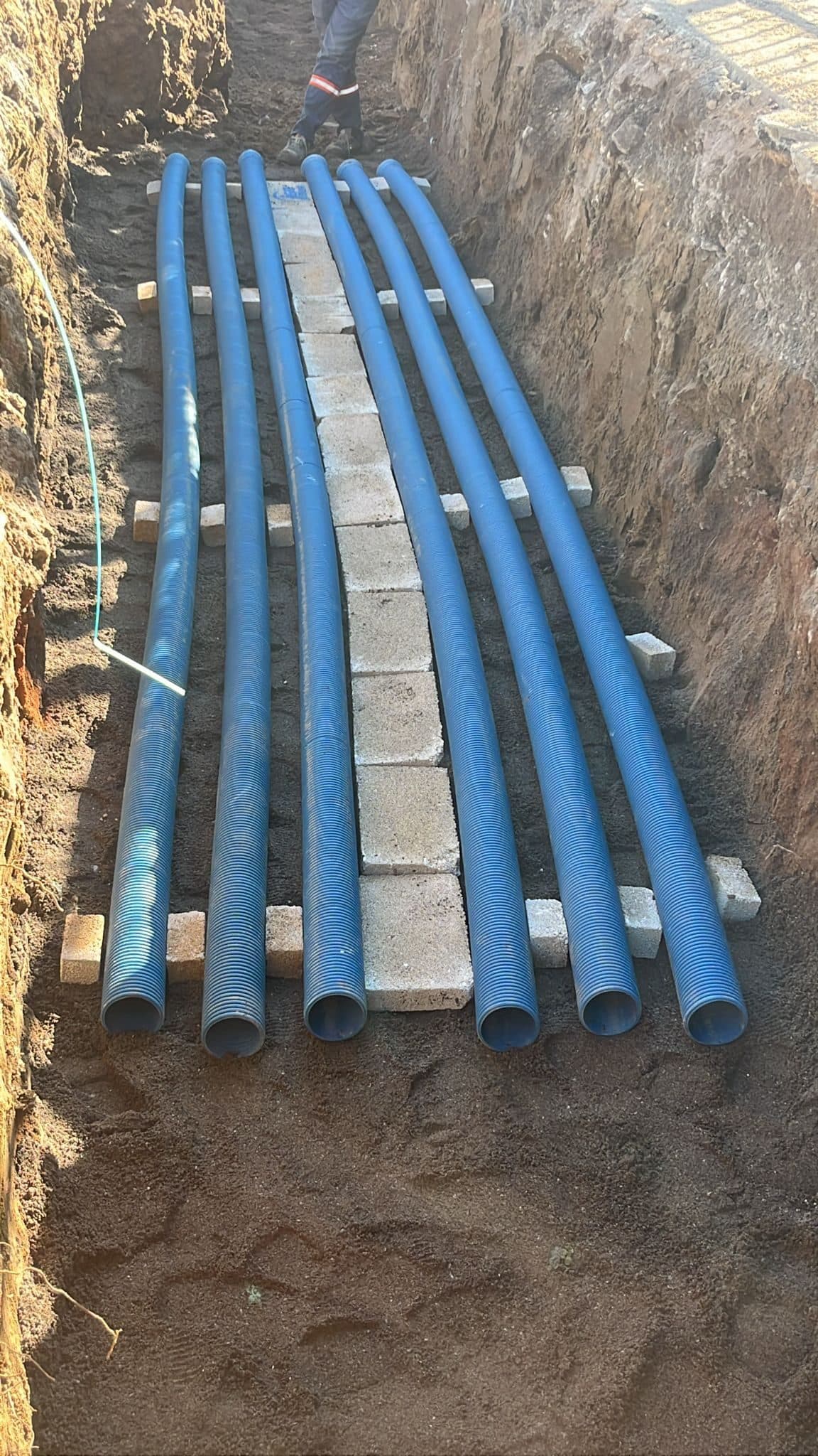 Kanal içinde beton takozlarla hizalanmış mavi PVC boru demeti