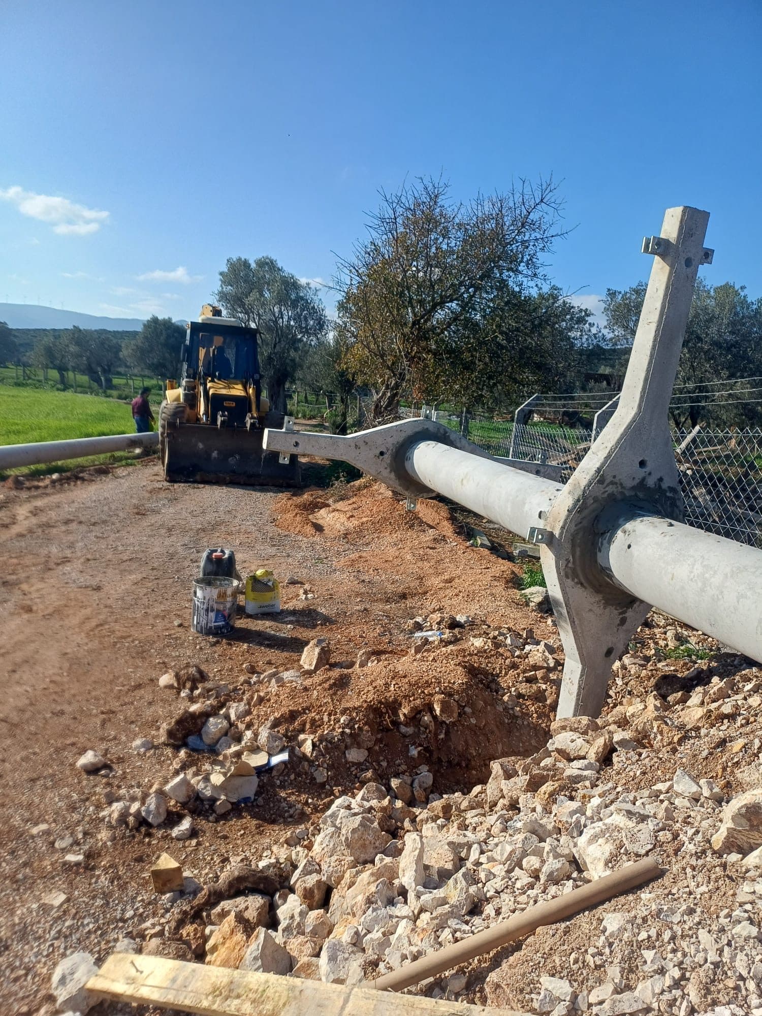 İş makinesiyle taşınan beton enerji direğinin saha üzerinde montaja hazırlanması